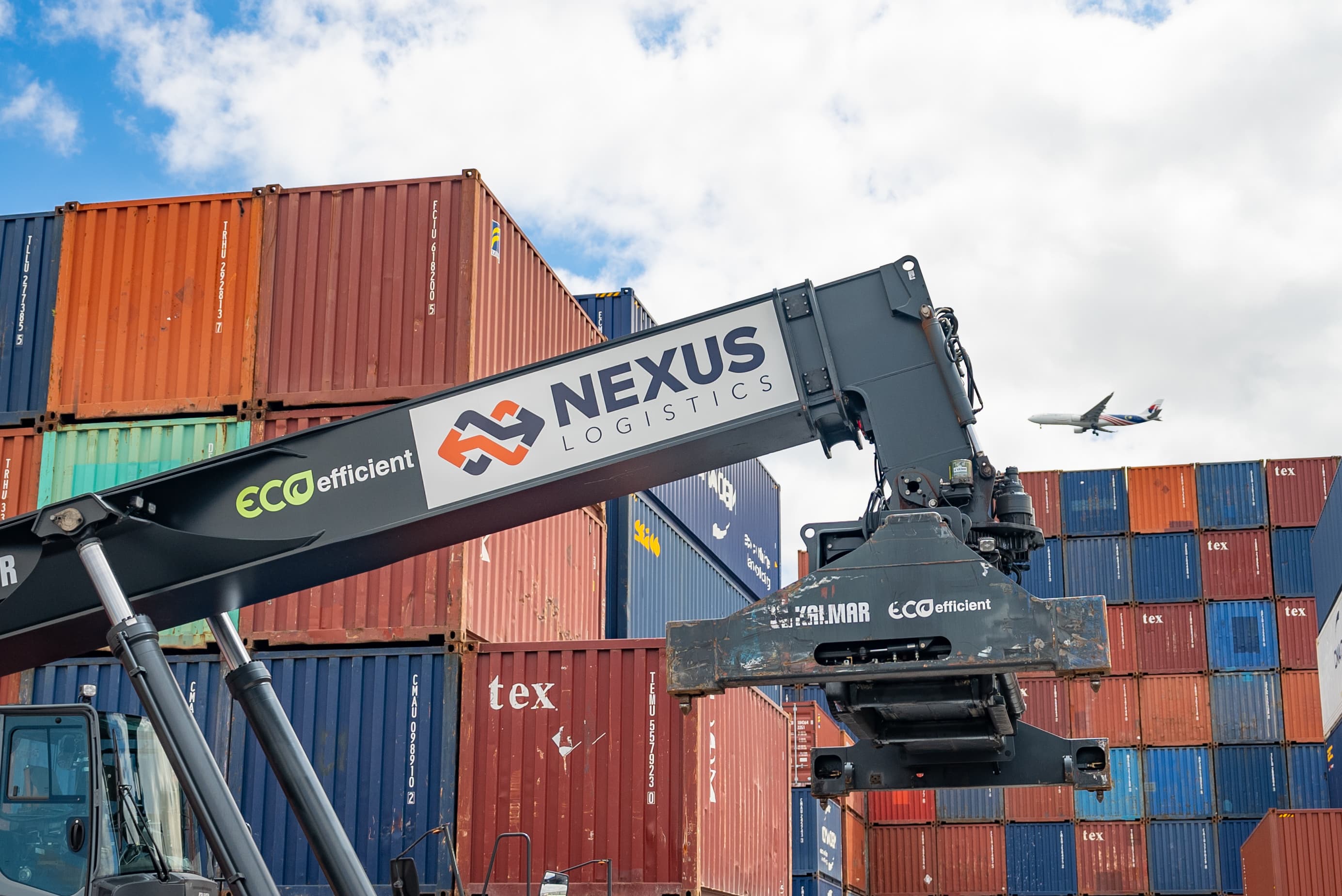 A reach-stacker branded with the Nexus Logistics logo lifting a shipping container
